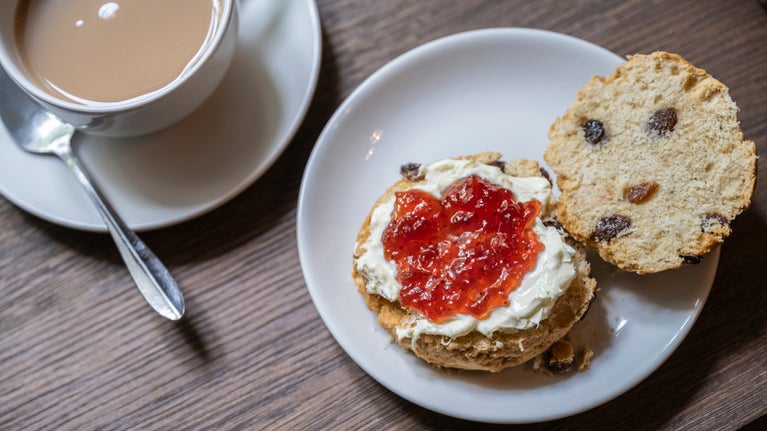 A scone spread with jam and clotted cream and a mug of tea on a table at Grantham House.